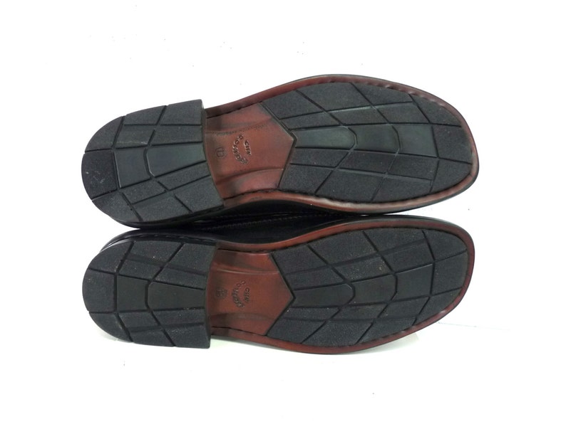 May include: The bottom of a pair of black leather shoes with a brown leather trim. The shoes have a textured rubber sole.