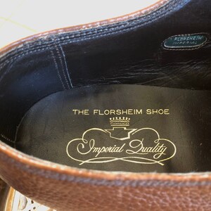 May include: Close-up of the inside of a brown leather shoe. The insole is black with gold lettering that reads "The Florsheim Shoe" and "Imperial Quality" with a crown design.