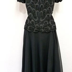 May include: A black formal dress with a beaded bodice and a flowing skirt. The bodice features intricate beadwork in a swirling pattern. The skirt is made of a lightweight, sheer fabric. The dress is suitable for special occasions.