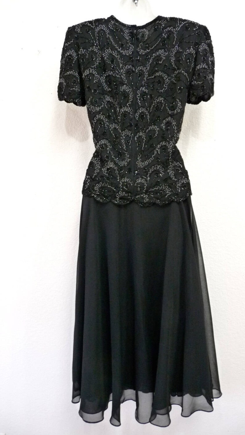May include: A black formal dress with a beaded bodice and a flowing skirt. The bodice features intricate beadwork in a swirling pattern. The skirt is made of a lightweight, sheer fabric. The dress is suitable for special occasions.