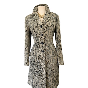 Può includere: Un cappotto lungo a maniche lunghe nero e beige con motivo a stampa di pelle di serpente. Il cappotto ha un colletto, una chiusura con bottoni e maniche lunghe.