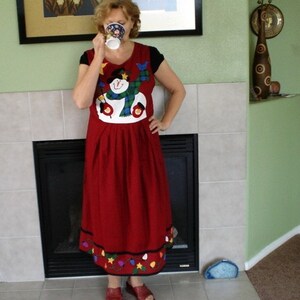 May include: A red dress with a snowman design and a white trim. The dress has a gathered skirt and a festive holiday theme.