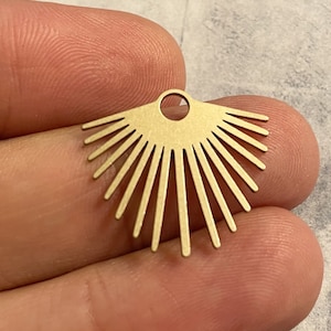 May include: A gold-toned metal fan-shaped charm featuring a series of thin, radiating lines extending from a central semi-circular base. The piece includes a small circular loop at the top center for attachment, showcasing a flat, smooth finish.