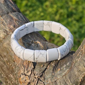 May include: A white and grey marble-effect bracelet. The bracelet is composed of square beads with a marbled pattern. The bracelet is shown on a tree branch, with a blurred green backdrop.
