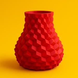 Puede incluir: Un jarrón rojo con un patrón geométrico en forma de cubo. El jarrón tiene una base ancha que se estrecha hacia un cuello y una abertura más estrechos. El jarrón está hecho de un material sólido y está sobre un fondo amarillo. El jarrón mide unos 25 cm de alto.