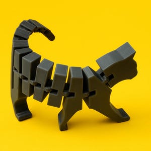 May include: A dark gray articulated cat figurine, posed on a bright yellow background. The cat's body is segmented, allowing for flexible posing. The tail is curved upwards, and the cat is in a walking position. The figurine is made of a matte material.