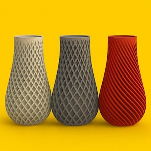 Op de afbeelding: Drie decoratieve vazen ​​naast elkaar. De vaas links is beige met een ruitpatroon. De middelste vaas is grijs met hetzelfde patroon. De vaas rechts is rood met een spiraalvormig ontwerp. Elke vaas heeft een unieke vorm.
