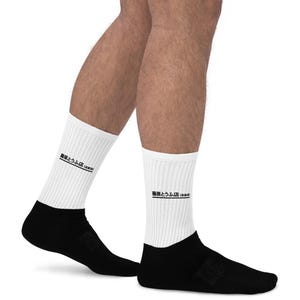 Könnte beinhalten: Weiße Socken mit schwarzem Text, der "bemerkenswert (auf Japanisch)" lautet. Die Socken werden an den Beinen eines Models gezeigt.