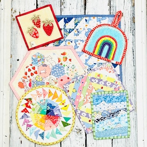 May include: A collection of colourful patchwork fabric squares with various designs, including strawberries, a rainbow, and flowers. The squares are arranged in a circular pattern and are perfect for crafting projects.