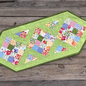 May include: A green quilted table runner with a floral patchwork design. The runner has a scalloped edge and is decorated with a repeating pattern of swirls.