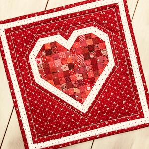 May include: A red and white quilted heart-shaped wall hanging with a white polka dot pattern. The heart is made of many small red fabric squares.