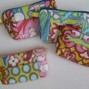 Puede incluir: Cinco bolsas de tela coloridas con cierres de cremallera. Las bolsas están hechas de tela de patchwork con varios patrones florales y geométricos en tonos de rosa, verde, marrón y amarillo.