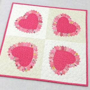 May include: A white quilt with four pink hearts. Each heart is made of pink fabric scraps and has a pink and white polka dot centre. The quilt is edged with a pink border.