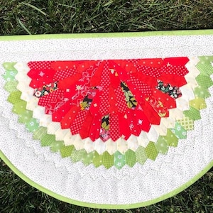 May include: A red, white and green watermelon-shaped quilt with a scalloped edge. The quilt is made of patchwork fabric and has a white background with small black dots.