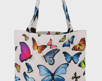 May include: White tote bag covered in colorful butterfly illustrations. The butterflies are in various sizes and colors, including pink, blue, orange, and yellow. The bag has matching handles with a butterfly pattern.