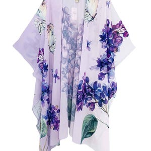 May include: A lightweight, open-front kimono in a soft lavender hue. The kimono features a vibrant floral and butterfly print in shades of purple, blue, and white. The design includes detailed illustrations of lilac flowers and butterflies, creating a delicate and artistic look.