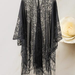 May include: Black lace kimono with a floral pattern and fringe trim. The open-front design features wide sleeves and a flowing silhouette. This elegant cover-up is perfect for layering over outfits.