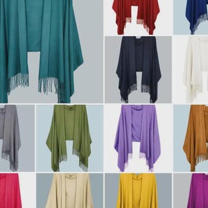 May include: A collection of shawls in various colors, including teal, red, navy, white, gray, olive green, purple, and gold. Each shawl has a draped design with a cowl neck and fringe detailing along the bottom edge. The shawls are displayed against a neutral background.