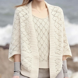 May include: Cream-colored knit cardigan and matching top with a diamond pattern. The cardigan has three-quarter sleeves and a draped front. The top has a scoop neck. The outfit is paired with gray pants and wrist warmers.