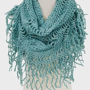 May include: A teal-colored, open-weave scarf with a fringed edge. The scarf is draped over a white mannequin, showcasing its texture and design. The knitted pattern creates a delicate, airy look, perfect for adding a touch of style.