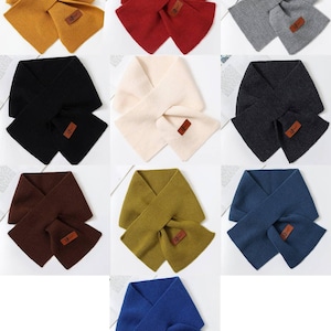 May include: A collection of nine solid-colored scarves, each with a matching pocket. Colors include mustard yellow, red, gray, black, cream, charcoal, brown, olive green, and blue. Each scarf has a small, rectangular leather tag.