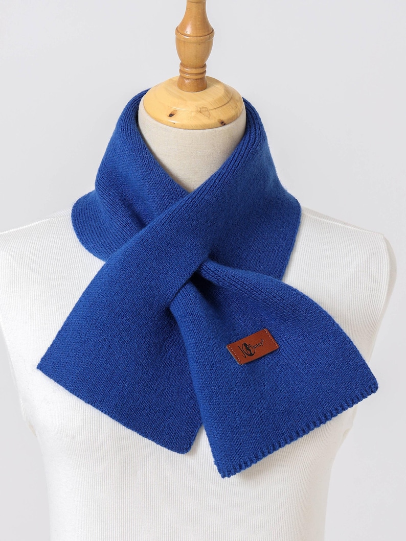 Puede incluir: Bufanda azul brillante de punto, exhibida en un maniqu&iacute;. La bufanda tiene una etiqueta de cuero marr&oacute;n con un logotipo. La bufanda est&aacute; doblada y drapeada, resaltando su textura y color. Un accesorio de invierno.