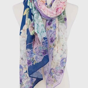 May include: A floral scarf in shades of blue, purple, pink, and white, draped over a mannequin. The scarf features a vibrant floral pattern with a dark blue border. The lightweight fabric is ideal for spring or summer.