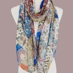 May include: A lightweight scarf featuring a multi-colored patchwork design with intricate floral, paisley, and geometric patterns in shades of blue, cream, orange, and deep red. The fabric displays a repeating motif across the entire surface.