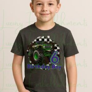 K&ouml;nnte beinhalten: Ein dunkelgraues T-Shirt mit einem gr&uuml;nen Monstertruck-Design, der Zahl 6 und dem Text "Birthday Boy" in Blau und Gr&uuml;n. Das T-Shirt wird von einem jungen Mann in blauen Jeans getragen.
