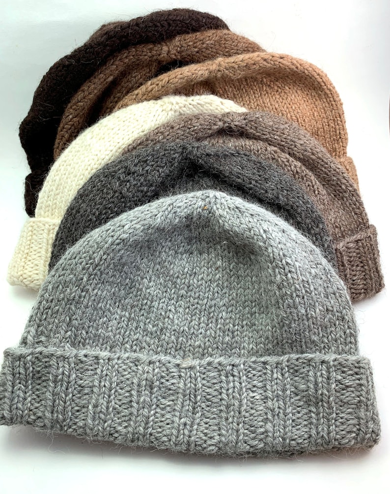 Puede incluir: Cinco gorros de lana tejidos en diferentes tonos de marr&oacute;n, gris y blanco. Los gorros est&aacute;n apilados uno encima del otro.