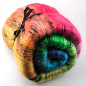 May include: A rolled wig in a vibrant rainbow of colours, including pink, orange, yellow, green, and blue. The wig is tied with a black ribbon. The bright colours create a striking visual effect.