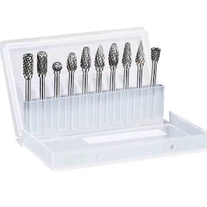 May include: A set of ten metal rotary burr bits in a clear plastic storage case. The burrs have various shapes, including cylindrical, ball, and conical, and are designed for use with rotary tools. The case is open, displaying the tools.