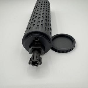 May include: A black cylindrical container with a textured surface and a removable lid. The container has a small hole on the side and a threaded opening on the bottom.