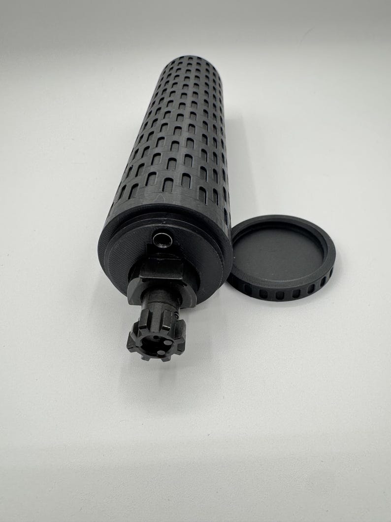 May include: A black cylindrical container with a textured surface and a removable lid. The container has a small hole on the side and a threaded opening on the bottom.