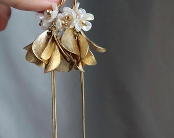 May include: Gold-toned earrings featuring a floral design. The earrings have small white flower clusters at the top, with textured gold leaf-shaped dangles and long, delicate gold chains. The earrings are designed to dangle.