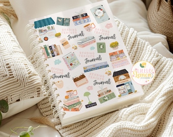 May include: A spiral-bound journal with a white cover featuring colorful illustrations of books, mugs, and decorative elements. The words "Reading Tracker Journal" are repeated throughout the design. The journal is open, displaying the pages, and rests on a cream-colored knitted blanket.