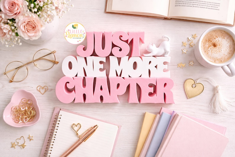 May include: A flat lay featuring a pink and white decorative sign that reads "JUST ONE MORE CHAPTER." The scene includes a cup of coffee, books, glasses, and stationery, all in soft, pastel colors. Gold accents add a touch of elegance.