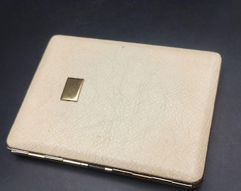 May include: Cream-colored rectangular case with a textured surface and a gold-colored rectangular accent. The case has a hinged design with a gold-colored metal frame. The case is closed.