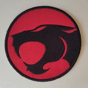 May include: A white ceramic mug with a black handle and the text "But First, Coffee" in a black, bold font. The mug is sitting on a wooden surface. The mug is approximately 4 inches tall.