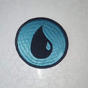 May include: Embroidered patch featuring a stylized water drop design. The patch has a circular shape with a teal blue background and a black water drop in the center. The patch is outlined with a black border.