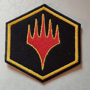 May include: Black, hexagonal patch with a yellow border and a red, stylized trident design. The patch is embroidered with a textured appearance, suitable for application on clothing or accessories. The design is centered on the patch.