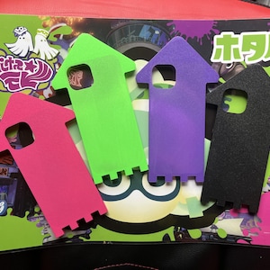 May include: Four colorful, arrow-shaped cutouts in pink, green, purple, and black, arranged on a game-themed background. The background features a green and purple design with Japanese text and cartoon characters.