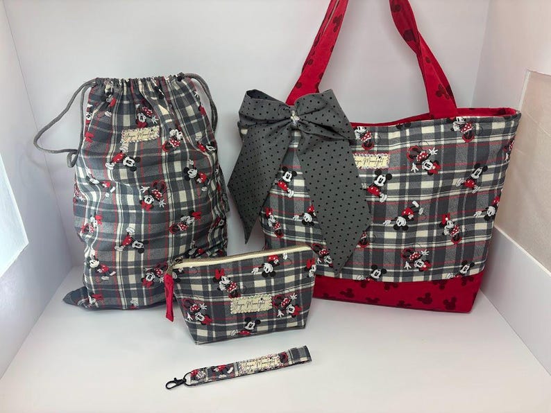 Puede incluir: Un conjunto de bolsos y accesorios de cuadros grises con un estampado de Minnie Mouse. El conjunto incluye una bolsa con cord&oacute;n, un bolso tote con un lazo grande, una peque&ntilde;a bolsa con cremallera y una pulsera. El bolso tote tiene detalles y asas rojas.