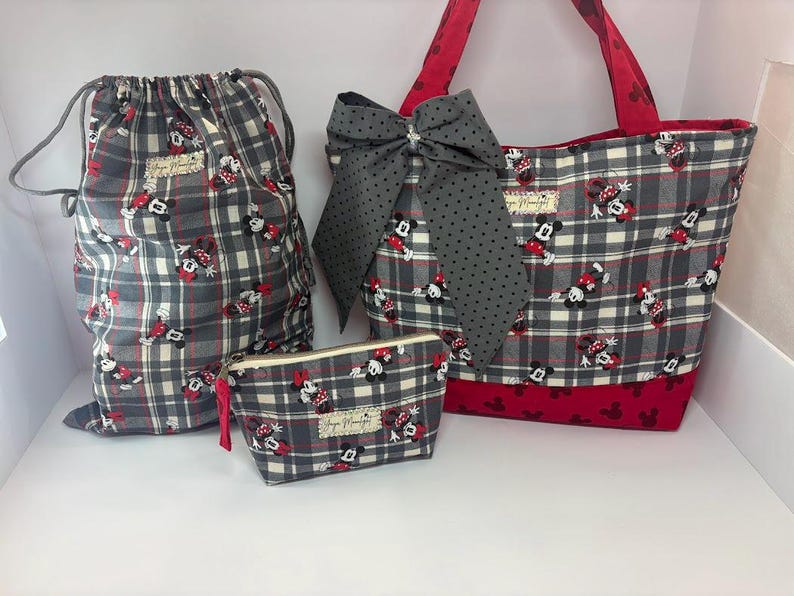 Puede incluir: Un conjunto de cuatro bolsas de tela a juego con un estampado de cuadros grises con detalles en rojo y dise&ntilde;os de Minnie Mouse. El conjunto incluye una bolsa con cord&oacute;n, un bolso tote con un lazo grande y una bolsa con cremallera. El bolso tote tiene asas rojas y una base roja.