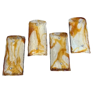 May include: Set of four amber glass wall sconces with a white marbled pattern. Each sconce has a rectangular shape and features a textured surface.