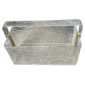 Può includere: Una scatola rettangolare di vetro trasparente con una superficie strutturata e increspata. La scatola ha una maniglia ed è tenuta insieme da accenti metallici color ottone. Il design ricorda gli stili vintage o art déco.