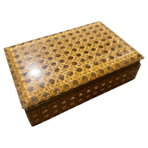 May include: Rectangular box with a woven rattan top and sides. The box has a clear, glossy finish over the rattan, giving it a polished look. The sides are a darker brown, creating a contrast with the lighter rattan.