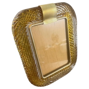 May include: An amber-coloured photo frame with a textured design. It features a gold-coloured metal border and a wooden backing. The frame has a curved, organic shape. The frame's dimensions are in centimetres.