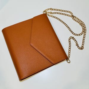 Puede incluir: Un bolso de mano de cuero marrón estilo sobre con una correa de cadena dorada.