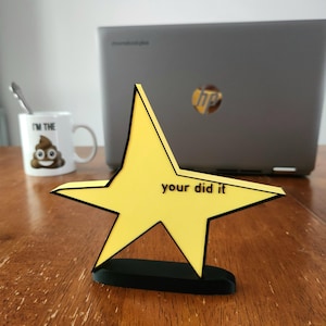 May include: A yellow star-shaped award with a black base and the text "you did it" on the front.